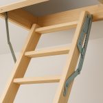 A close-up view of a wooden loft ladder installed in a ceiling, with metal hinges visible.